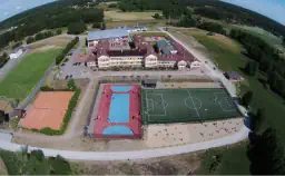 Widok orlika z lotu ptaka. Widoczne bosiko do koszykówki, piłki nożnej, kort to tenisa, stadion, a także szkoła