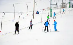 Ludzie podchodzący pod górkę w nartach. W tle znajduje się sporo śniegu.