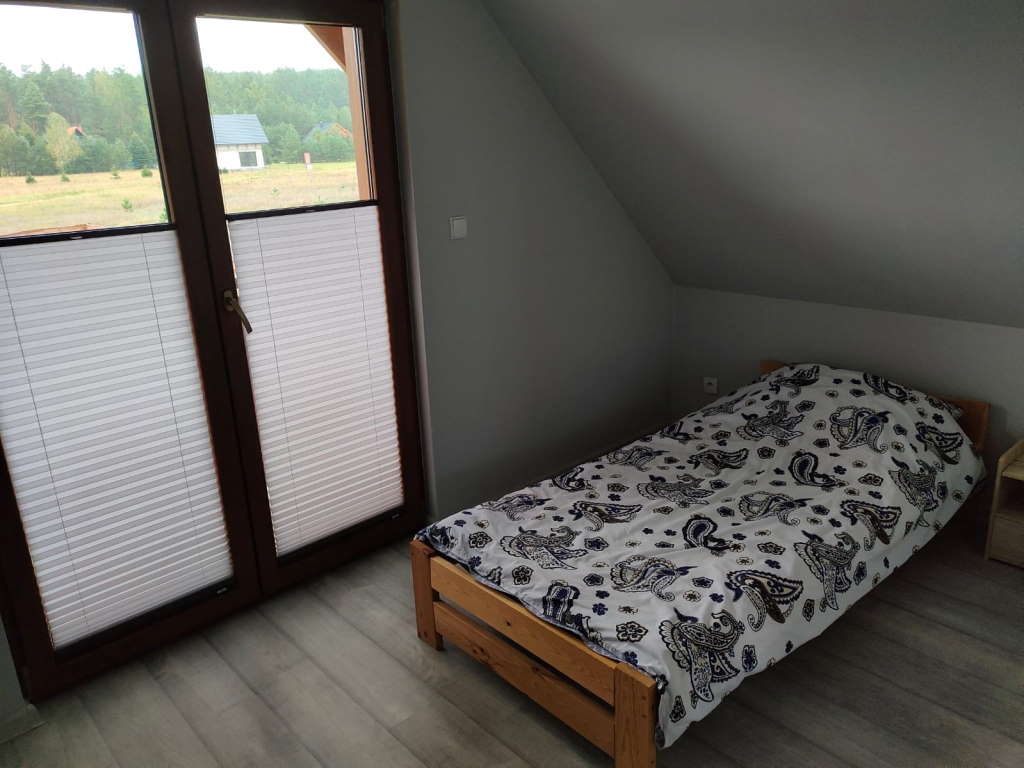Sypialnia - widoczne pojedyncze łóżko, mała szafka i drzwi balkonowe